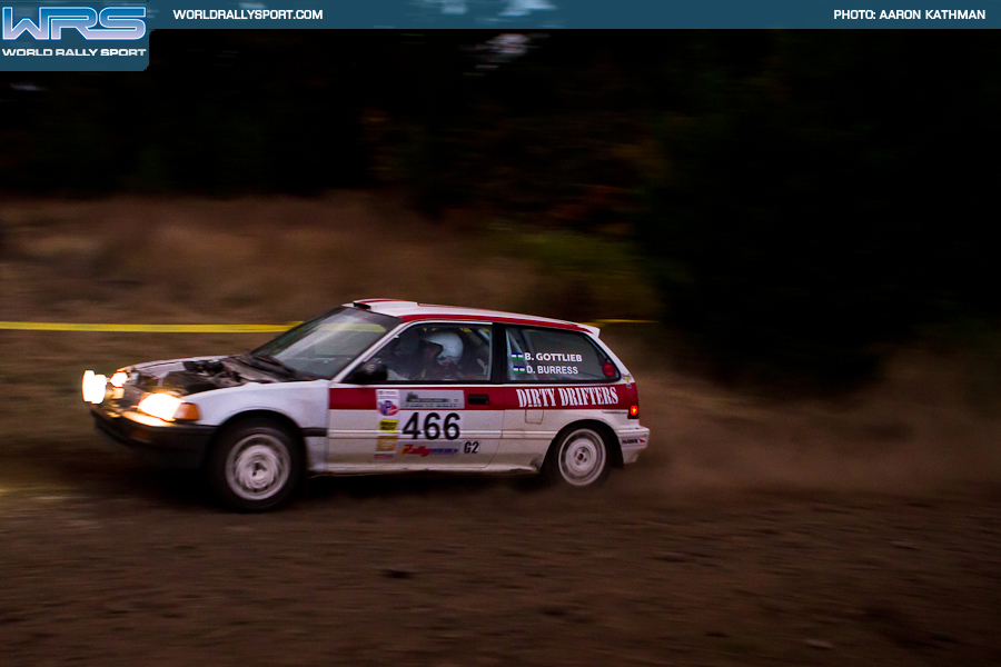 an older honda civic curises by with no hood on a gravel road